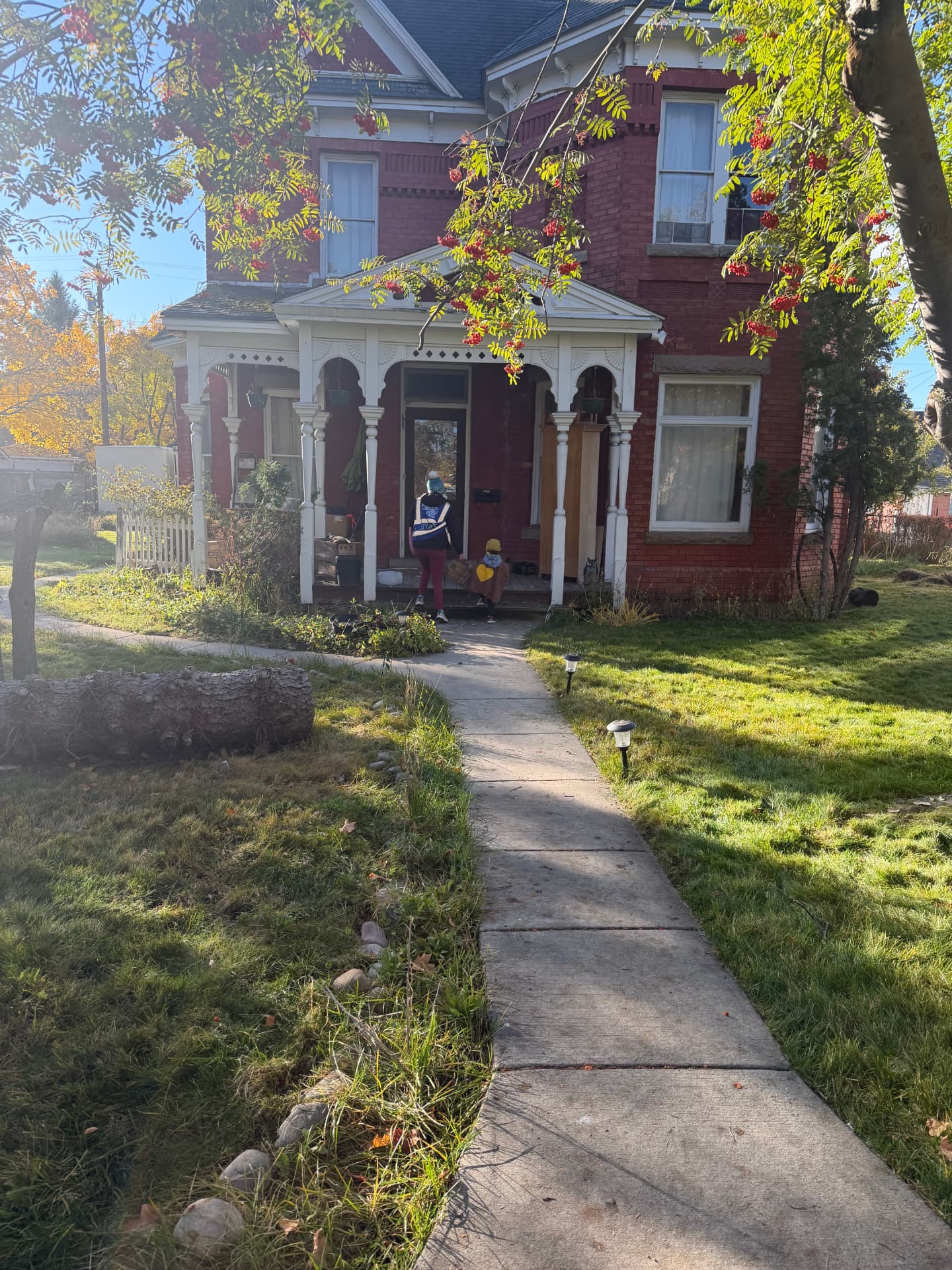 A learner in a cape stands at a neighbor's front door to deliver a Trick-or-Can Food Drive bag