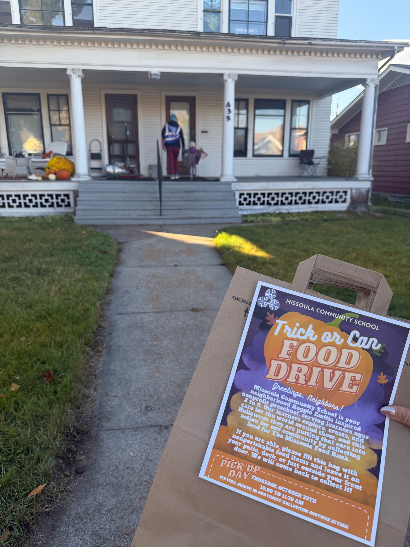 A Trick-or-Can Food Drive bag with its flyer waits on a neighbor's front porch